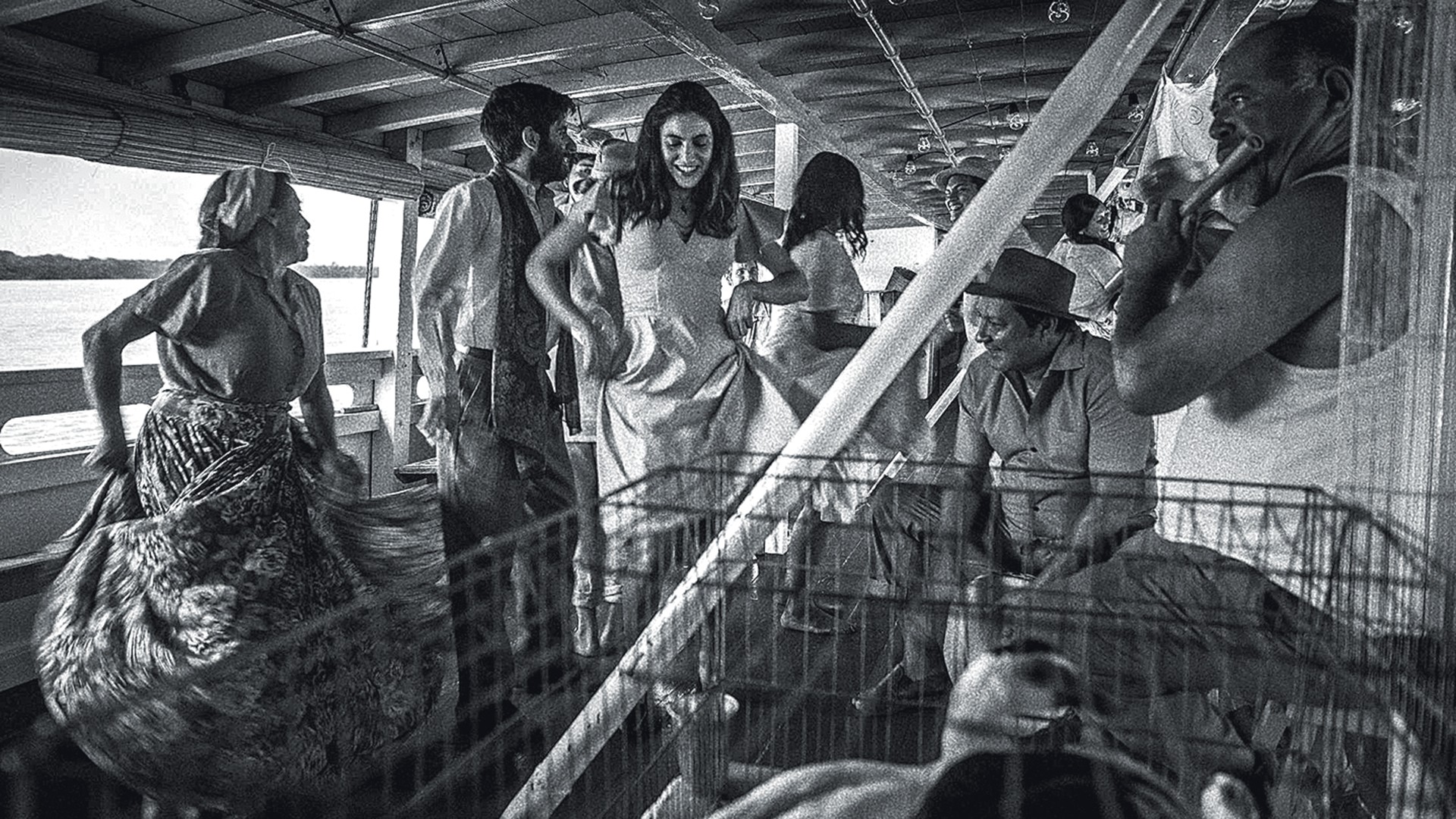Pessoas dançando e tocando música em um barco, com uma mulher de vestido rodopiando e um homem tocando flauta, em preto e branco
